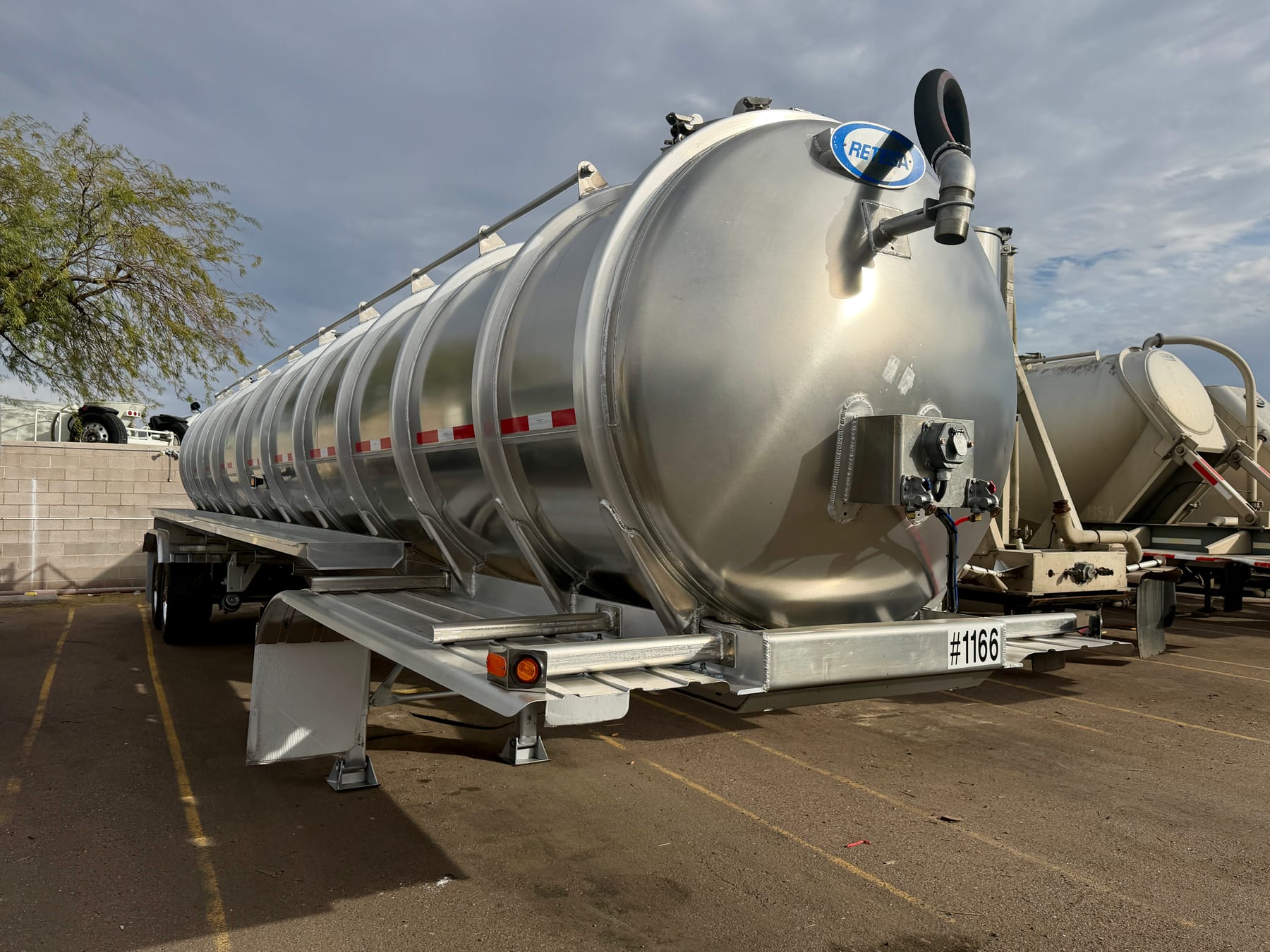 Silver liquid-hauling tanker trailer parked in an equipment yard.